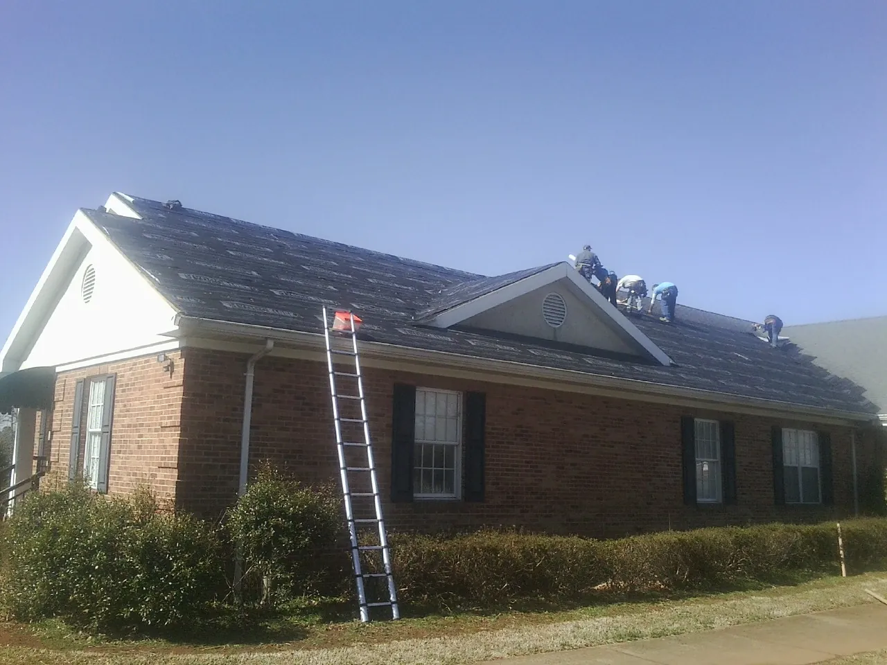 Crew tearing shingles off a brick ranch roof with a ladder set — Metal Roof Repair work by our crew in Barry
