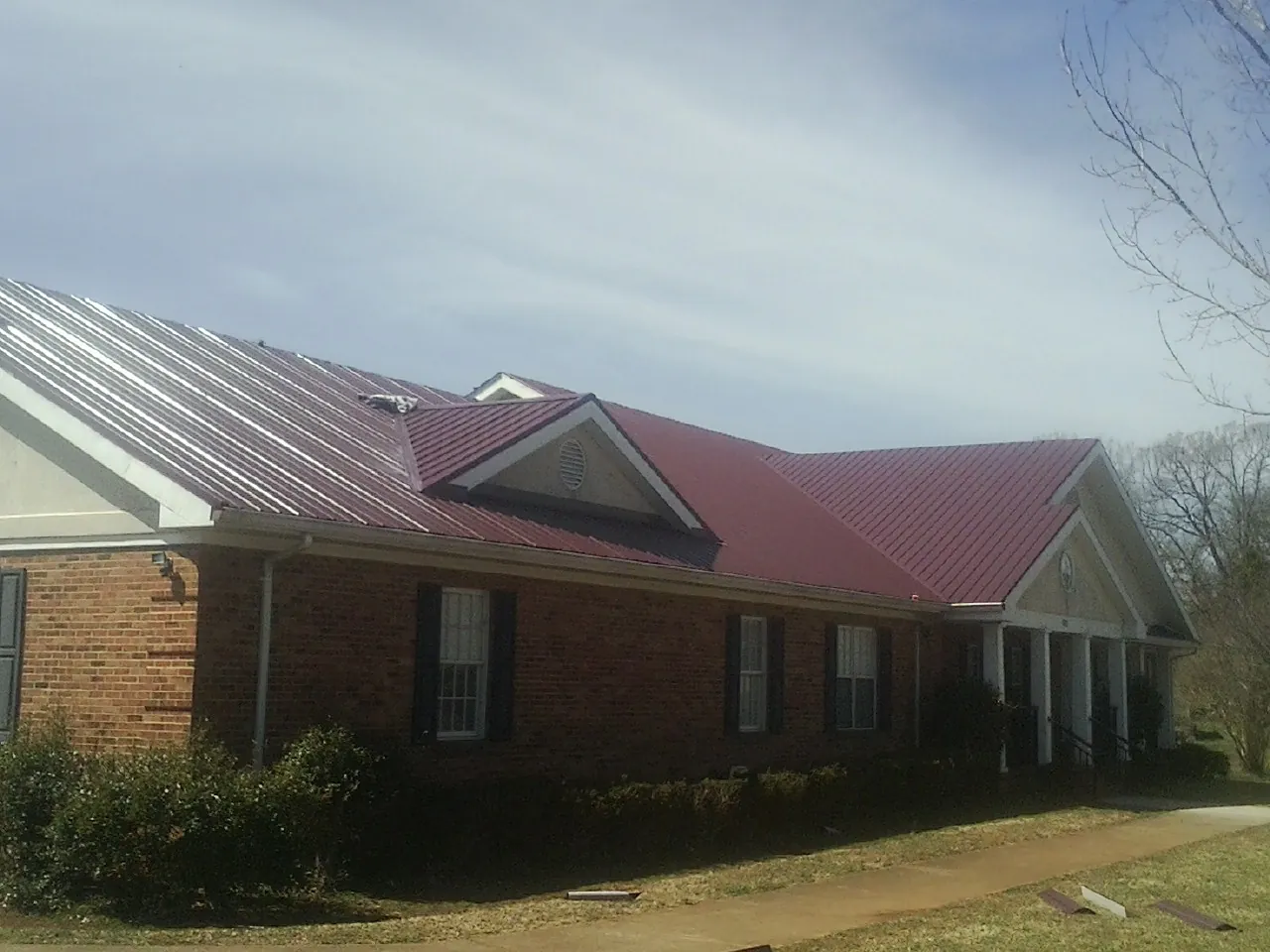Red metal roof with gabled entries on a long brick building, from a Hail Damage Roof Repair job in Barry