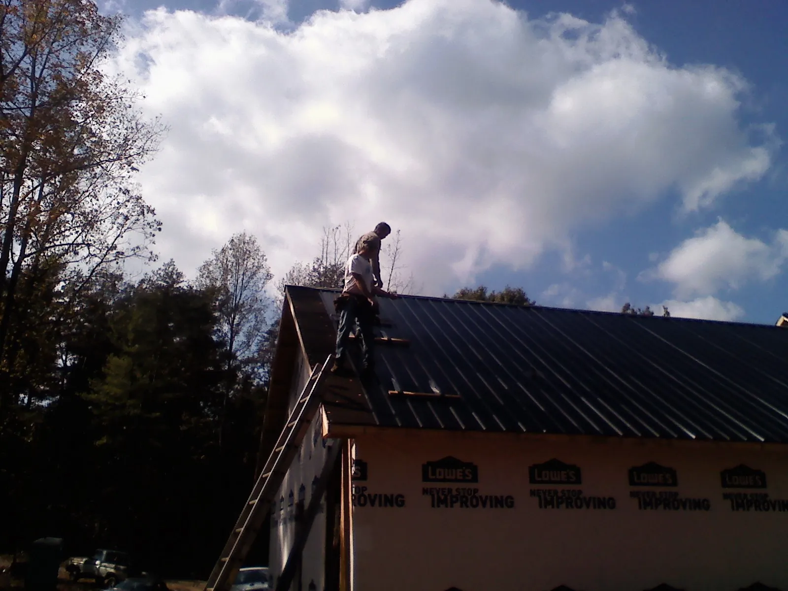 Roofer fastening dark metal panels high against a cloudy sky in Barry